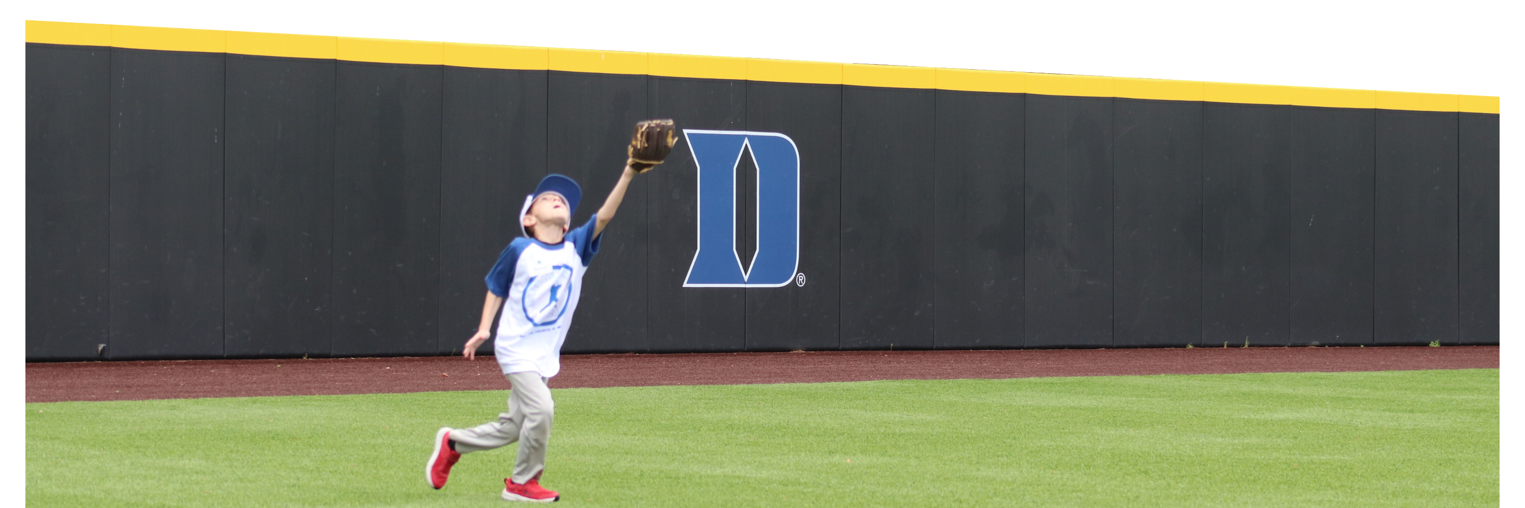 boy reaches to catch a ball on Duke baseball field