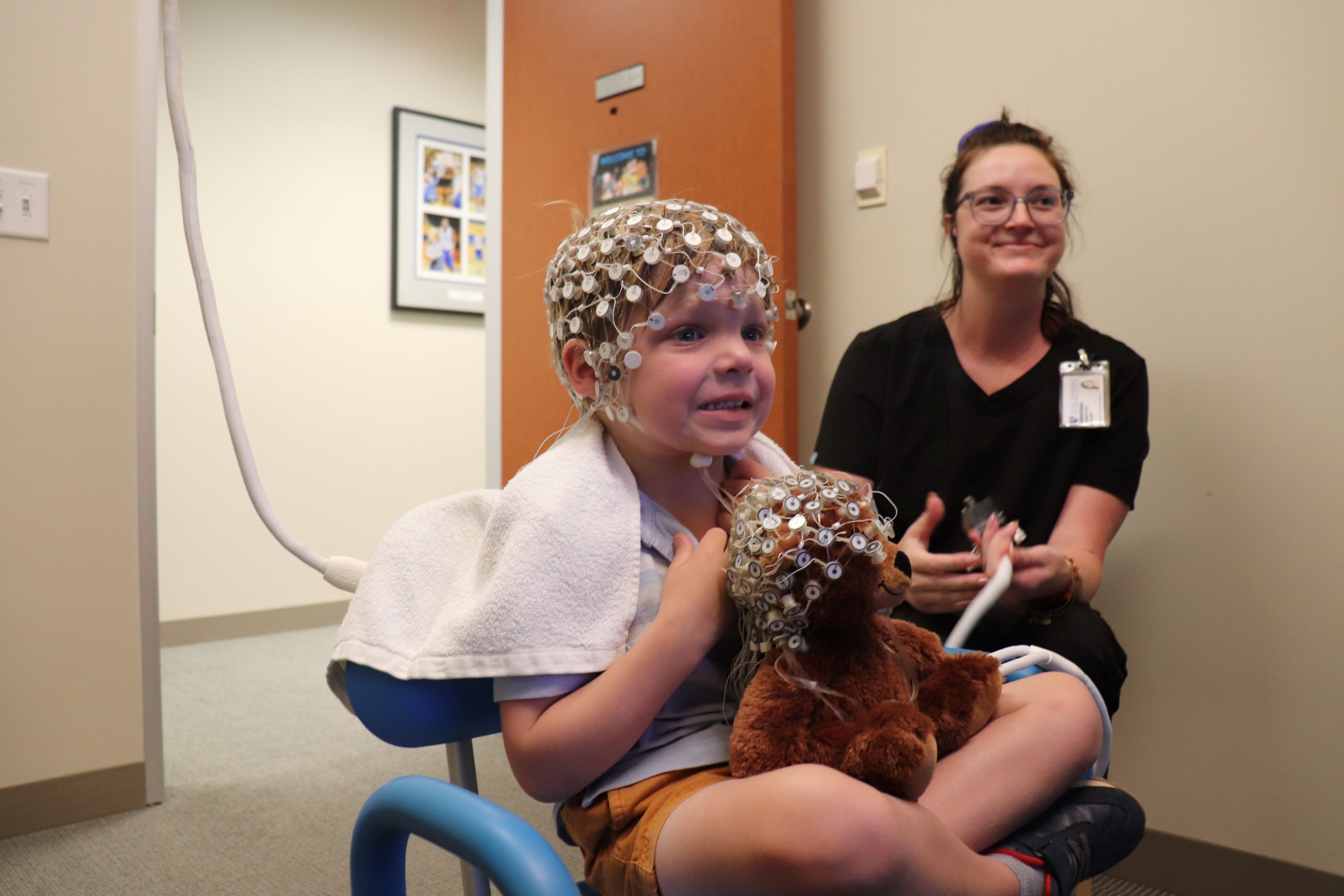 child wearing an EEG net and holding a teddy bear that is also wearing an EEG net
