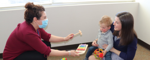therapist showing musical intstrument to child while mother holds child