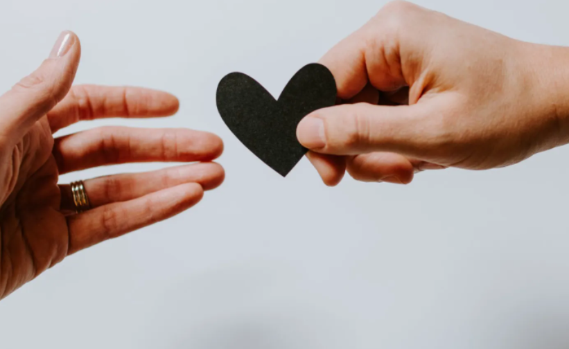 close up of two hands. one is giving a paper heart to other