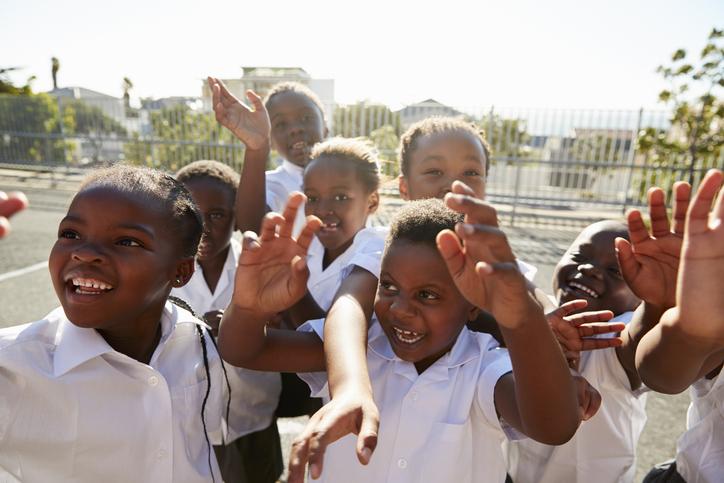 A group of Black children in matching white school uniforms play on a playgroud