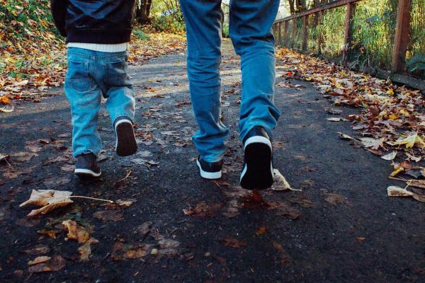 Man and boy walking on a forest path in autumn. Only legs and feet are shown. 