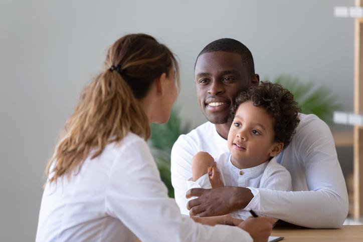 A man holds a young child while talking to a medical provider
