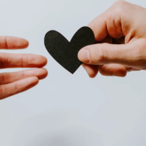 close up of two hands. one is giving a paper heart to other